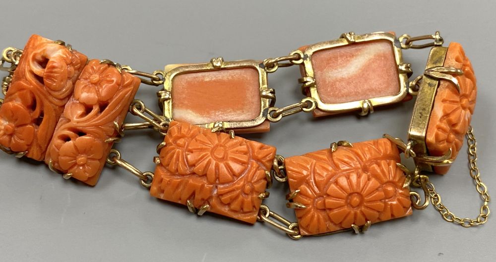An early 20th century yellow metal seven stone coral panel set bracelet, carved with flowers, approx. 16.5cm, gross 19.6 grams.